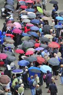 Pilgrims with umbrellas in the rain praying in front of the grotto at the Sanctuary of Our Lady of Lourdes