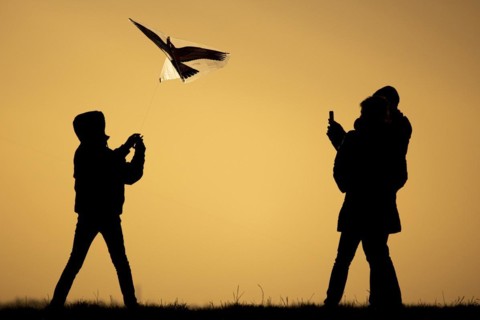 The silhouette of three people emerges while flying a kite in front of sunset in Berlin