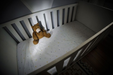 Symbolic photo on the subject of child abuse. A teddy bear sits in an empty cot. Berlin