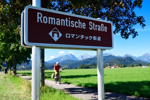 Cyclist in front of sign Romantic Road with translation in Japanese