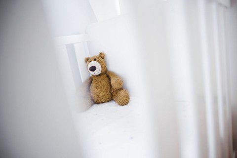 Symbolic photo on the subject of wanting a child. A teddy bear sits in an empty cot. Berlin