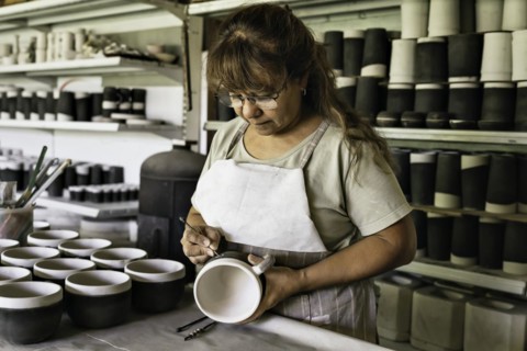 Middle-aged woman craftswoman with apron making the sgraffito on a piece of pottery