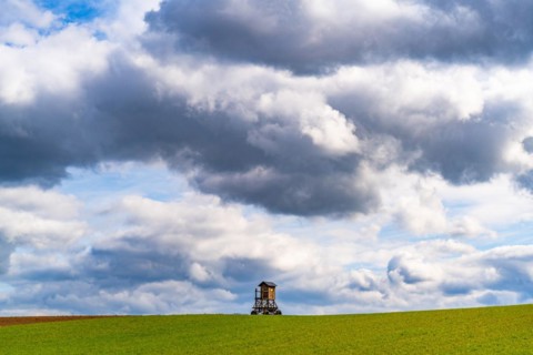 Mobile raised hide in an empty field under dramatic clouds