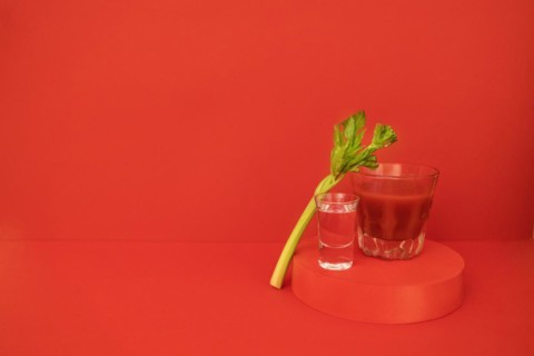 A glass of red cocktail with greens on the podium. Stylish alcohol tomato beverage Bloody Mary on a red background. Delicious drinks concept. Copy space