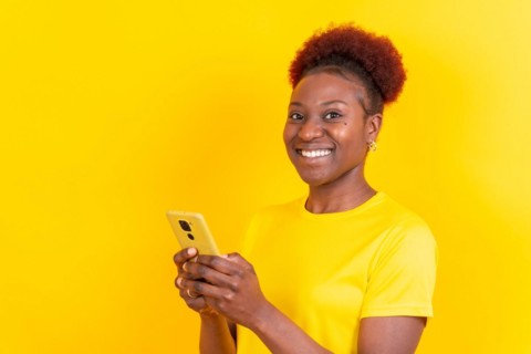 Young african american woman isolated on a yellow background smiling with the mobile phone