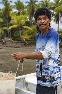 Man looking at the camera preparing his net to fish in his boat with palm trees in the background