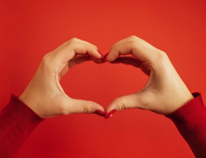 Female hands make a heart shape. Hands of a young white girl with a beautiful bright red manicure. Close up. Valentine day concept. Red background