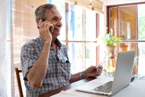Mature business man smiling and talking on phone in front of laptop