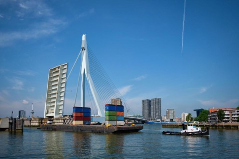 Tug boat towing barge with containers under open bascule part of Erasmusbrug bridge in Nieuwe Maas river. Rotterdam