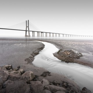 Long exposure of the famous bridge Ponte Vasco da Gama at low tide on the river Tejo with a small water tributary in Lisbon