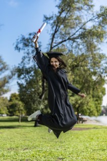 Happy graduated girl in a black gown jumping while holding her diploma
