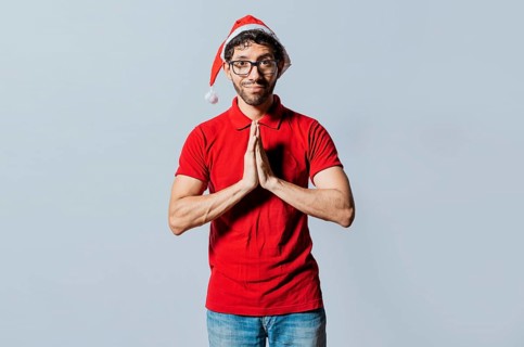 Man in christmas hat with hands together making a wish isolated. Guy with hands together making a christmas wish