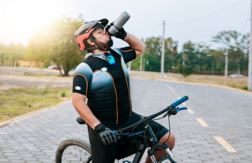 Tired cyclist drinking water outdoors. Chubby cyclist on his bike drinking water
