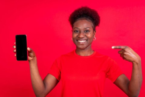 Young african american woman isolated on a red background with mobile pointing gesture