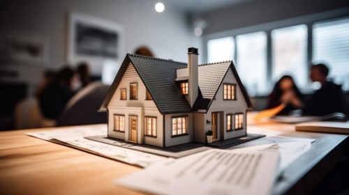Small model house resting on real estate documents as buyers discuss their agreement