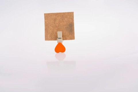 Heart shape clothespin attached to a note paper on a white background