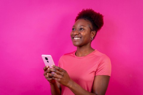 Young african american woman isolated on a pink background smiling with the mobile phone