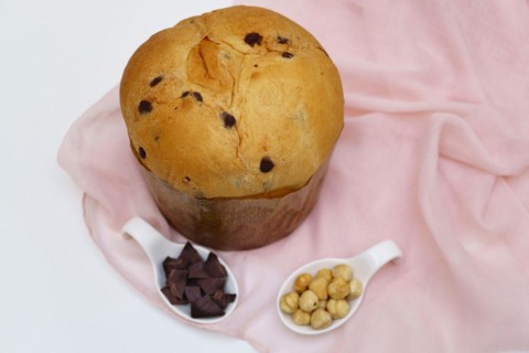 Panettone on a pink cloth and white background with ceramic spoons with hazelnuts and chocolate