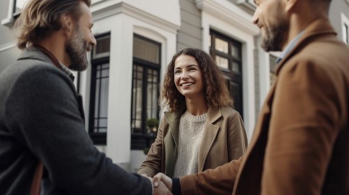 Young adult couple shaking hands with their real estate agent in front of A new house