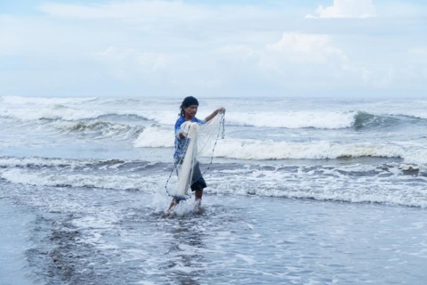 Fisherman walking with his net into the sea looking at the camera