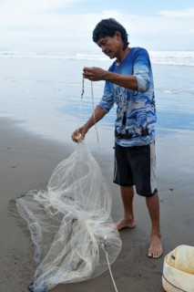 A rustic Central American fisherman with moustaches and curly hair prepares his net on the seashore. Vertical portrait