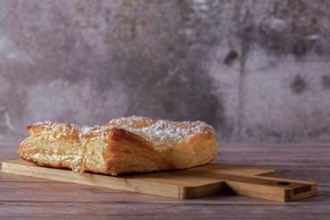 Close-up of an apple tart with shredded coconut on a wooden board with gray background and copy space