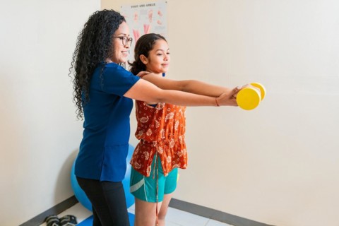 Rehabilitation physiotherapy in fitness ball. Physiotherapist helping patient with dumbbell sitting on rehabilitation ball