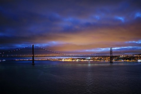 View of 25 de Abril Bridge famous tourist landmark of Lisbon connecting Lisboa and Almada on Setubal Peninsula over Tagus river in the evening twilight. Lisbon