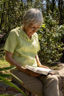 Elegant mature woman reading a book in a park. Vertical portrait