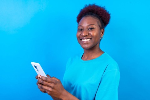 Young african american woman isolated on a blue background smiling with the mobile phone