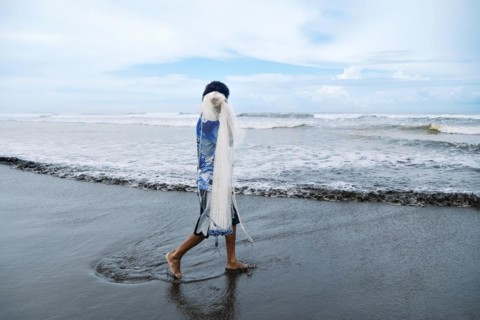 An unrecognizable fisherman walks with his net along the shore of the Pacific Sea