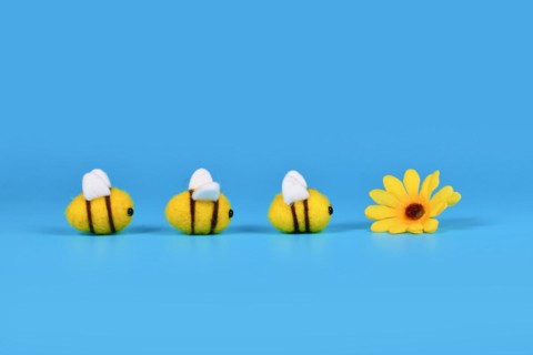 Felt bees in a row crawling towards yellow flower on blue background with copy space