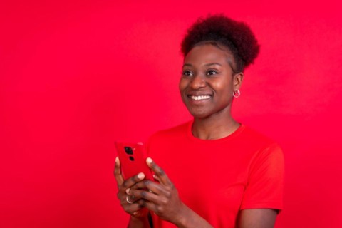 Young african american woman isolated on a red background smiling with the mobile phone