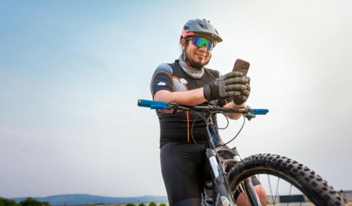 Male cyclist with helmet using cell phone. Cyclist on his bike texting with phone outdoors. cyclist man with helmet and glasses texting on cell phone outdoors