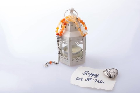 The word EID EL FITR on torn paper beside a lantern and prying beads