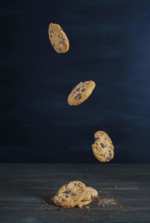 Chocolate cookies falling in a row on a wooden table with dark background and copy space