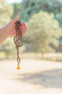 Woman's hands holding a hindu japa mala illuminated by sun in meditation in the countryside at sunset