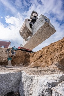 Excavator grab with stone on construction site