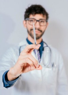 Close up of doctor holding a syringe isolated. Smiling doctor holding a syringe on isolated background
