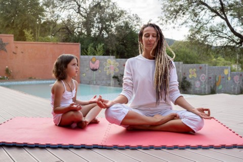 Blonde rasta mother with her little daughter sitting in lotus position. Meditation and relaxation