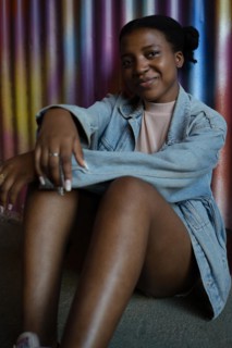 Pretty young African American girl smiling looking at the camera seated leaning her back against a colorful metal wall