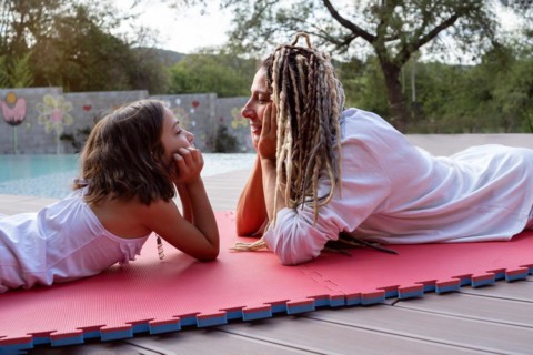 Rasta beautiful woman and a little girl lie on a mat face to face and look at each other
