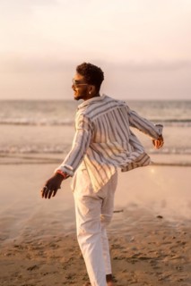 Portrait of attractive black ethnic man enjoying summer vacation by the sea feeling free and dancing