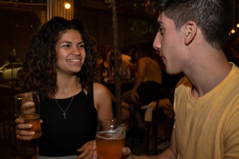 Young latina woman smiling and chatting with a young man in a bar drinking beer. Meeting of an online date. Blurred background