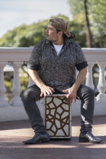 Hispanic man shot hands playing percussion with a Flamenco box sitting on top of it in a park