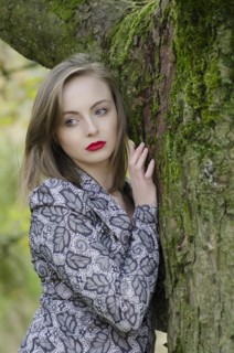Pensive young woman leaning against a tree looking away