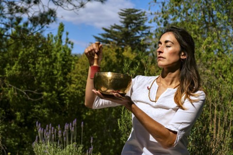 Young woman feeling the vibration of a Tibetan singing bowl outdoors. Sound therapy and meditation