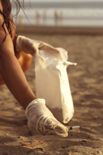 Volunteer girl collecting cigarette butts on the sand. Out-of-focus sunset background. Marine pollution destroying the environment