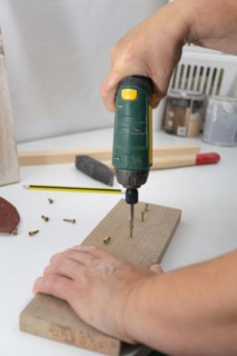 Woman with an electric screwdriver putting screws into a piece of wood