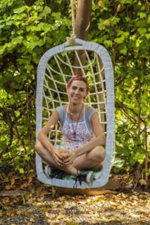 Smiling entrepreneur at her juice shop backyard resting on swing chair while drinking fresh detox juice